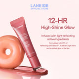 A tube of Laneige Glaze Craze Tinted Lip Serum in the shade Peach Glaze rests on a glossy surface, next to a peach-colored donut, showcasing its high-shine finish and highlighting the product's 12-hour glow and light-reflecting active ingredients.