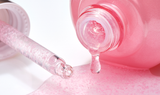 Pink, shimmering Laneige Glowy Makeup Serum flows from a dropper and bottle, showcasing its lightweight, hydrating texture for radiant and healthy-looking skin.