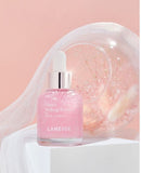 A bottle of Laneige Glowy Makeup Serum, shimmering pink with a delicate dropper, sits on a minimalist display, promising a radiant and healthy glow for long-lasting makeup.